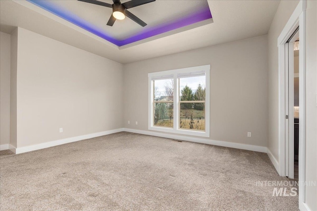 carpeted spare room featuring a tray ceiling, baseboards, and a ceiling fan