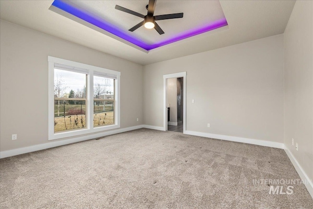 carpeted empty room featuring baseboards, a raised ceiling, and a ceiling fan