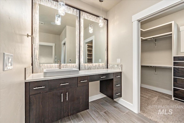 full bath featuring wood finish floors, vanity, a walk in closet, and baseboards