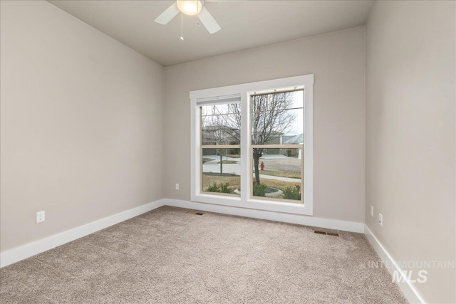 carpeted spare room with visible vents, baseboards, and ceiling fan