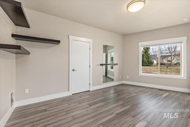 spare room featuring a textured ceiling, wood finished floors, visible vents, and baseboards