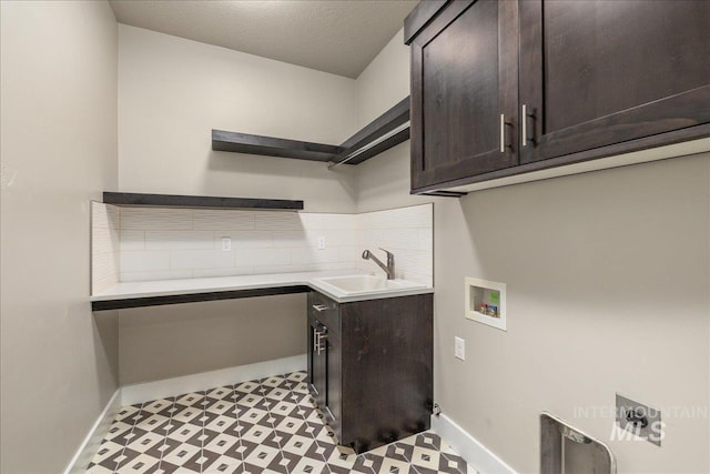clothes washing area featuring baseboards, light floors, cabinet space, a textured ceiling, and a sink