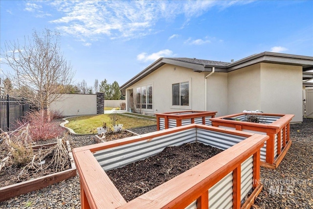 rear view of property featuring a garden, fence, and stucco siding