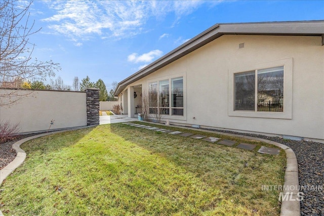 back of house with stucco siding, a yard, and fence