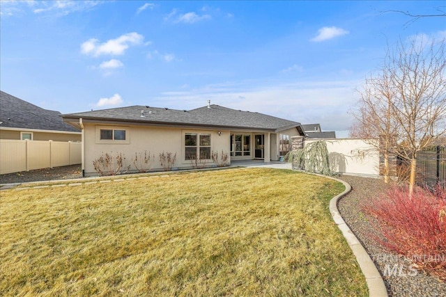 back of property with stucco siding, a lawn, a fenced backyard, a shingled roof, and a patio area