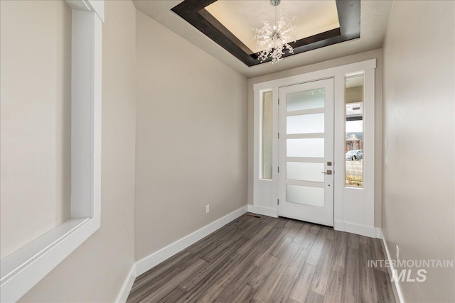 foyer entrance with baseboards, a raised ceiling, an inviting chandelier, and dark wood-style flooring