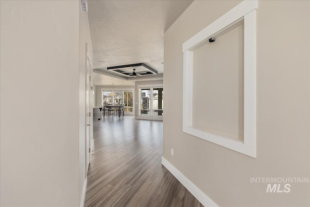 hall with wood finished floors, baseboards, and a textured ceiling