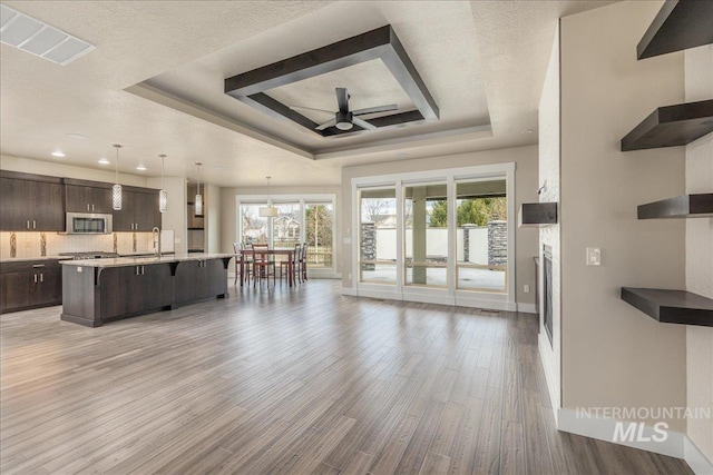 kitchen featuring open shelves, stainless steel microwave, dark brown cabinetry, a raised ceiling, and ceiling fan