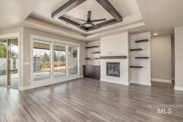 unfurnished living room with a raised ceiling, wood finished floors, and a healthy amount of sunlight