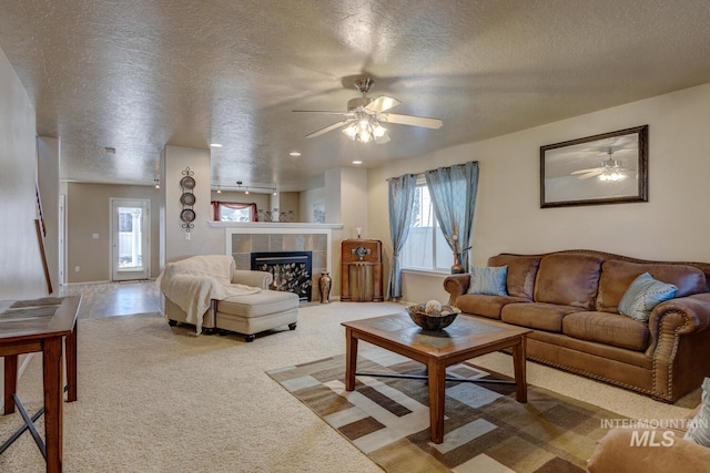 living room with a ceiling fan, light carpet, a textured ceiling, and a tiled fireplace