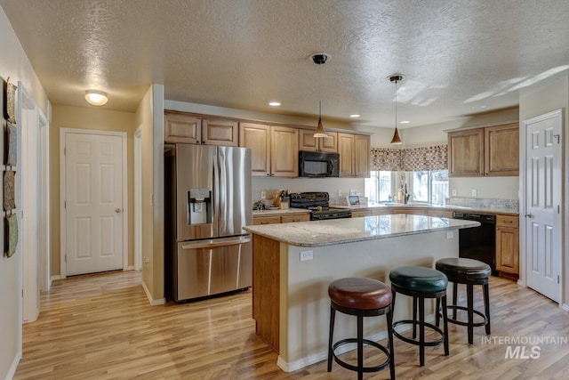 1587 N Firebrick Dr, Kuna, ID 83634 - kitchen with black appliances, a breakfast bar area, light wood-type flooring, and a center island