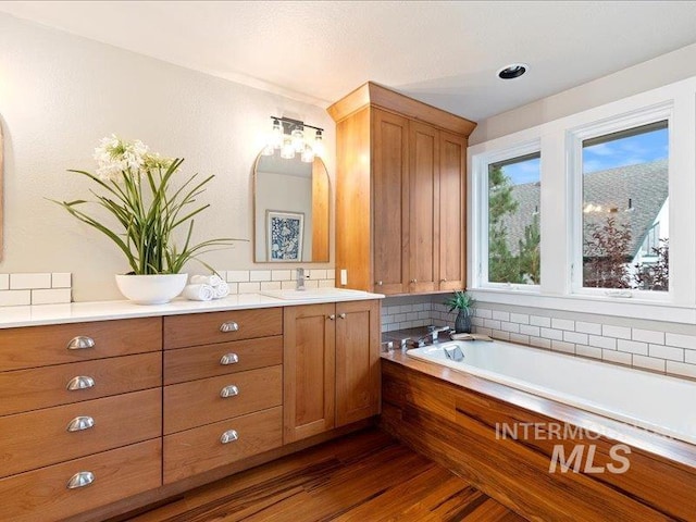 bathroom with vanity, hardwood / wood-style floors, decorative backsplash, and a tub