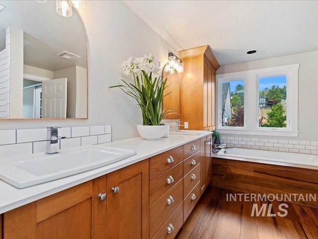 bathroom featuring vanity, tasteful backsplash, wood-type flooring, and a bath