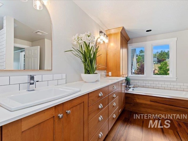 bathroom with double vanity, visible vents, a sink, wood-type flooring, and a garden tub
