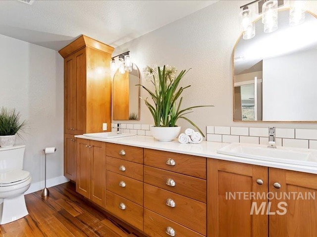 bathroom with double vanity, wood finished floors, toilet, and a sink