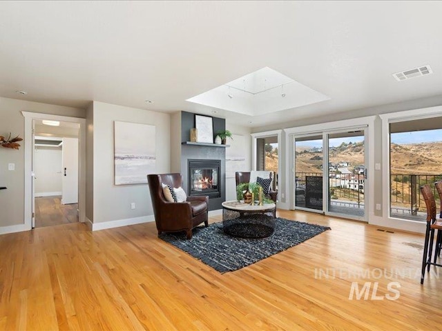 living room with a raised ceiling, wood finished floors, visible vents, baseboards, and a glass covered fireplace