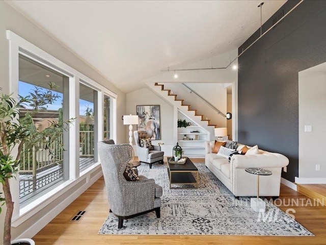 living area with wood finished floors, vaulted ceiling, visible vents, and stairway