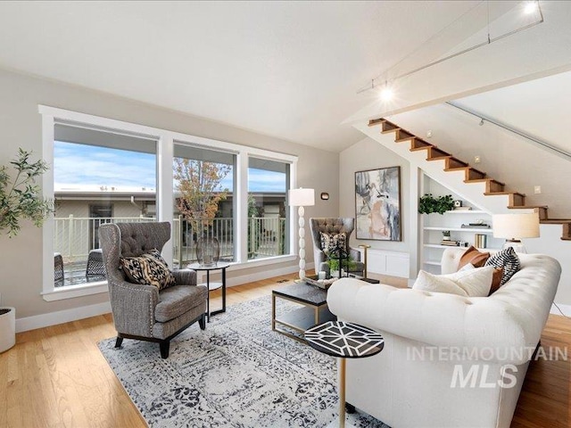 living area with stairway, vaulted ceiling, wood finished floors, and plenty of natural light