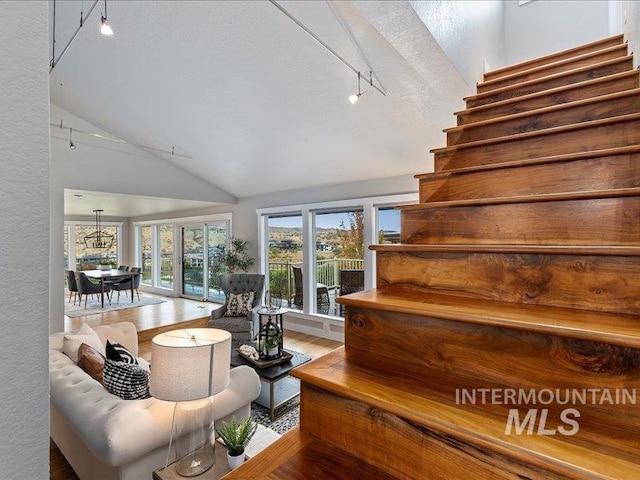 living room featuring track lighting, vaulted ceiling, stairs, and wood finished floors