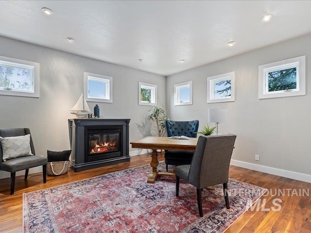 office space featuring baseboards, a glass covered fireplace, wood finished floors, and recessed lighting