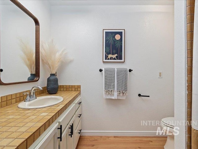bathroom with toilet, vanity, wood finished floors, and baseboards