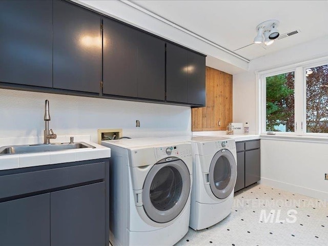 washroom with a sink, baseboards, visible vents, cabinet space, and washer and dryer