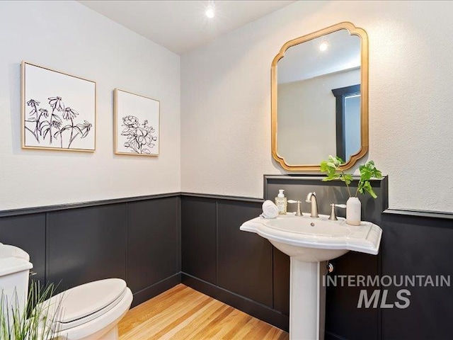 bathroom with wood finished floors, a decorative wall, toilet, and a wainscoted wall