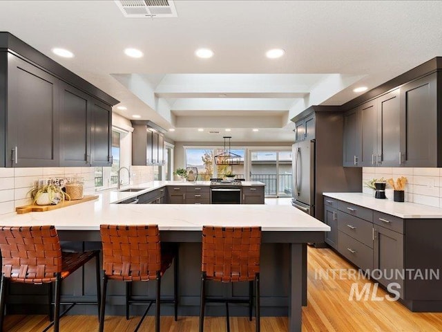 kitchen with a kitchen breakfast bar, kitchen peninsula, stainless steel appliances, sink, and light hardwood / wood-style floors