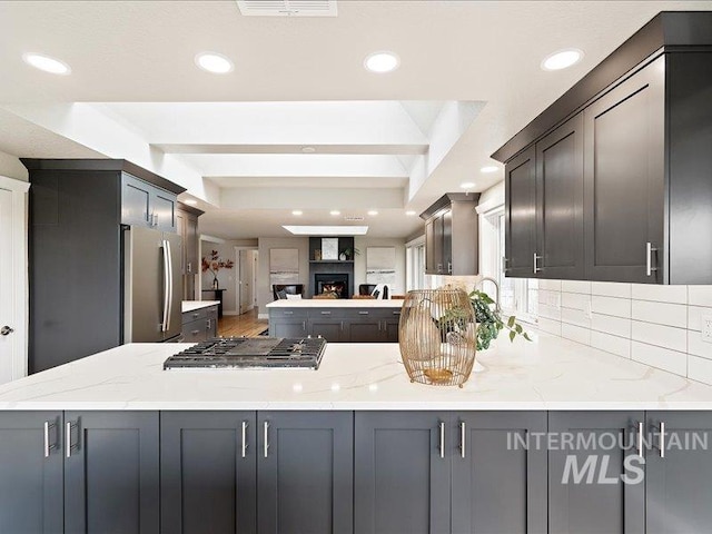 kitchen featuring stainless steel appliances, a peninsula, recessed lighting, light stone counters, and a fireplace