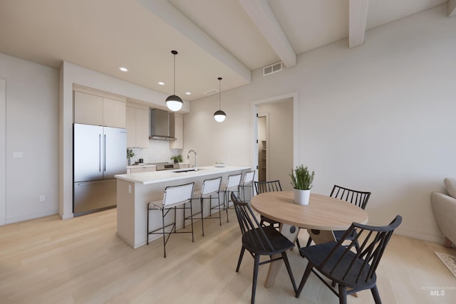 dining area with sink, light wood-type flooring, and beamed ceiling