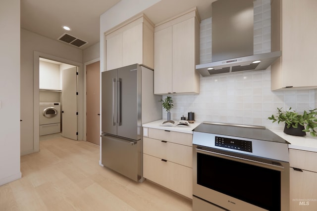 kitchen featuring washer / clothes dryer, appliances with stainless steel finishes, wall chimney range hood, and decorative backsplash