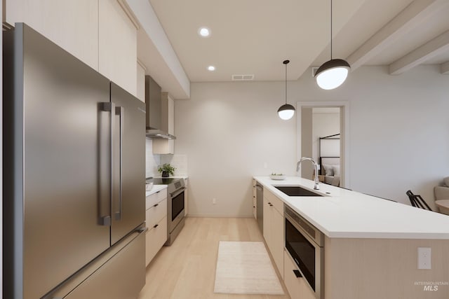 kitchen featuring appliances with stainless steel finishes, wall chimney exhaust hood, sink, light hardwood / wood-style flooring, and decorative light fixtures