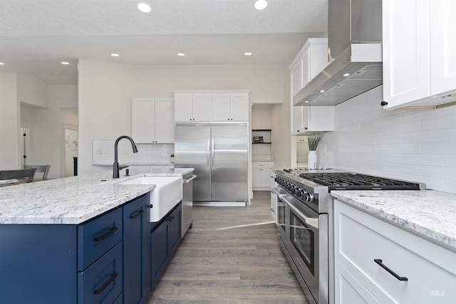 1910 W Campo Ln, Eagle, ID 83616 - kitchen featuring high quality appliances, wall chimney range hood, blue cabinets, white cabinetry, and recessed lighting