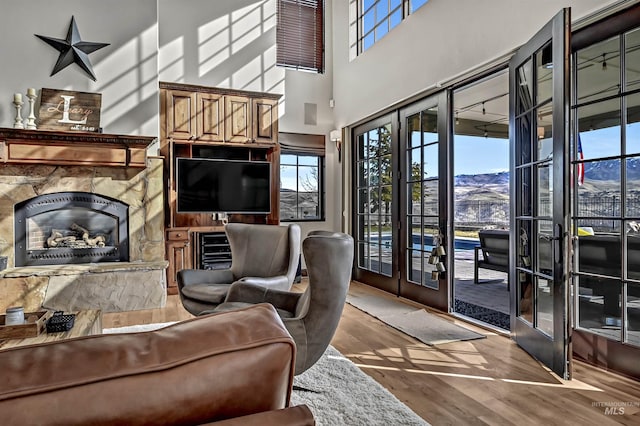 living area with beverage cooler, a premium fireplace, french doors, a high ceiling, and wood finished floors