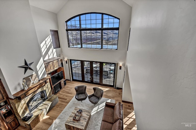 living area featuring a glass covered fireplace, high vaulted ceiling, baseboards, and wood finished floors