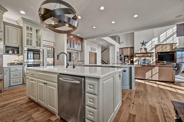 kitchen with open floor plan, light wood-style floors, a kitchen island with sink, and a sink