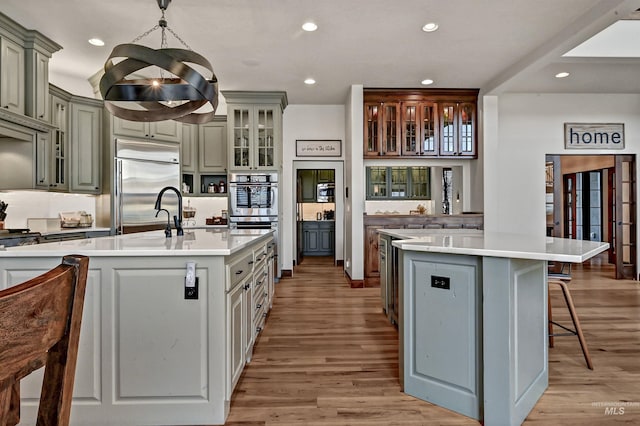 kitchen with a kitchen bar, a kitchen island with sink, light wood-style flooring, stainless steel appliances, and light countertops