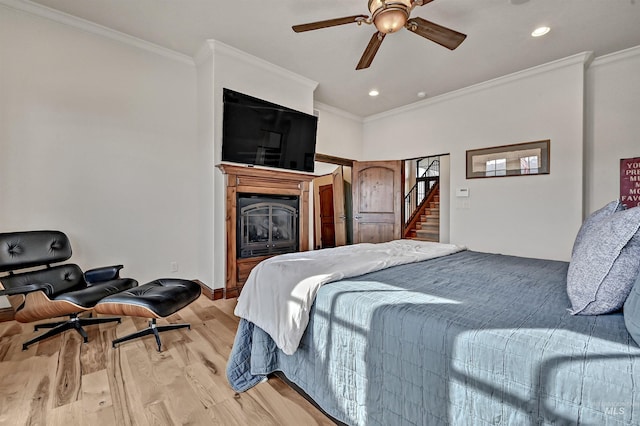 bedroom with a glass covered fireplace, light wood-type flooring, ornamental molding, and recessed lighting