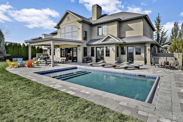 back of property featuring stucco siding, a chimney, a hot tub, a patio area, and a lawn