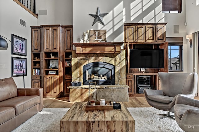 living area with a stone fireplace, a high ceiling, wood finished floors, and visible vents