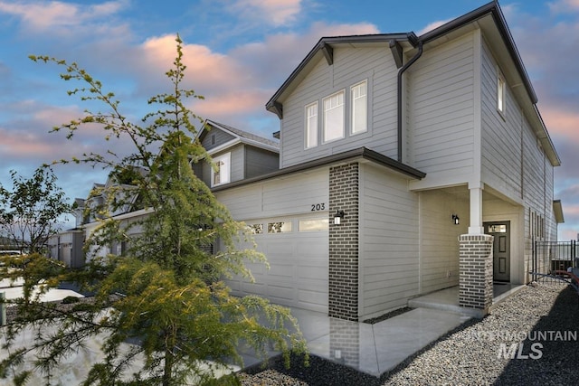 property exterior at dusk featuring an attached garage and brick siding