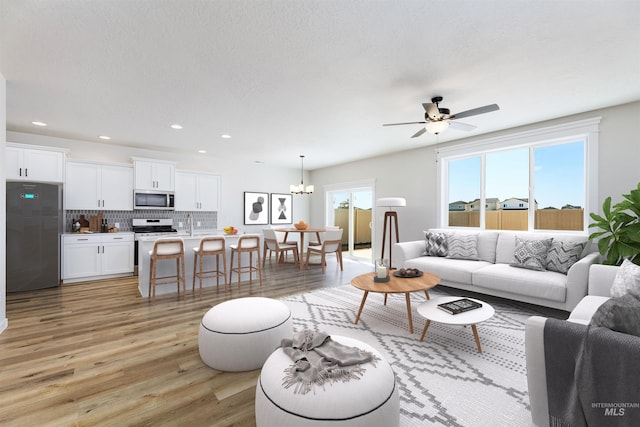 living room with ceiling fan with notable chandelier, light wood-type flooring, a textured ceiling, and recessed lighting