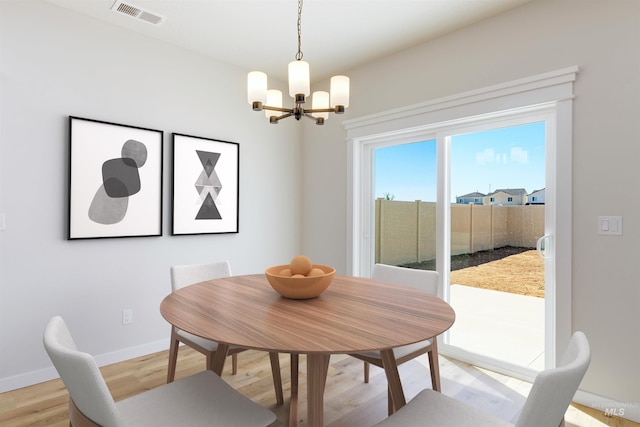 dining room featuring baseboards, light wood finished floors, visible vents, and an inviting chandelier