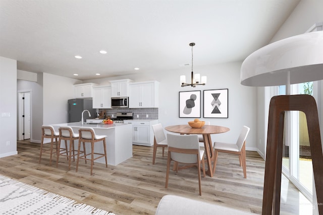 kitchen with stainless steel appliances, light wood finished floors, backsplash, and a center island with sink