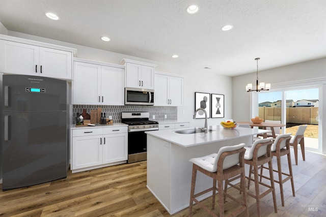 kitchen with stainless steel appliances, a sink, white cabinetry, decorative backsplash, and light wood finished floors