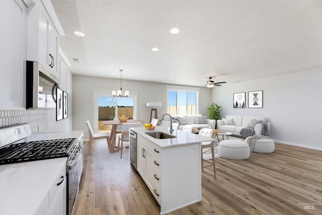 kitchen with appliances with stainless steel finishes, open floor plan, light wood-style floors, white cabinetry, and a sink