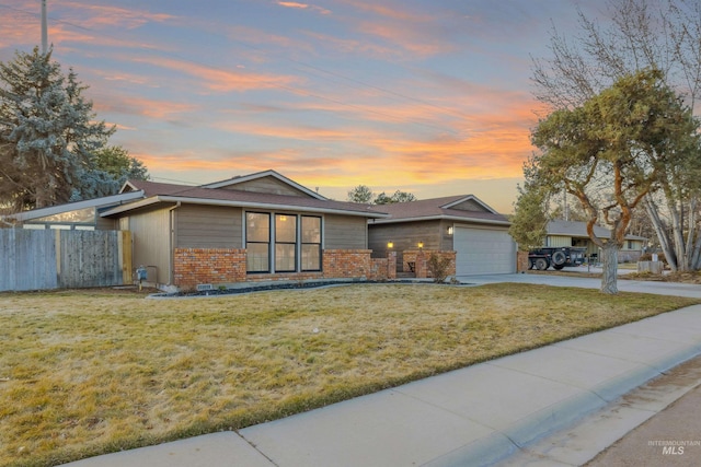 view of front of house with driveway, a garage, a lawn, fence, and brick siding