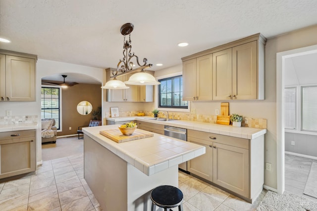 kitchen with arched walkways, tile countertops, a kitchen island, a sink, and a textured ceiling