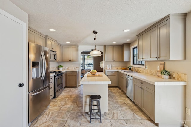 kitchen featuring stainless steel appliances, a center island, a sink, and tile countertops