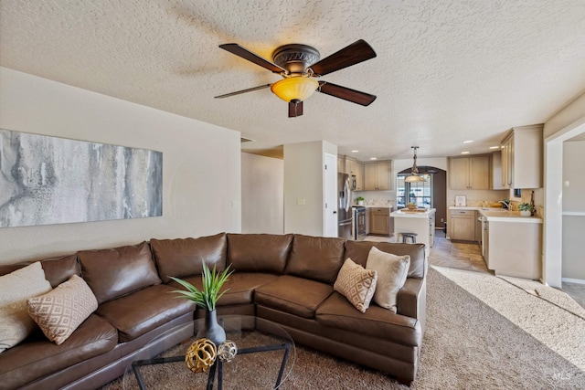 living room featuring a textured ceiling, recessed lighting, light colored carpet, a ceiling fan, and baseboards